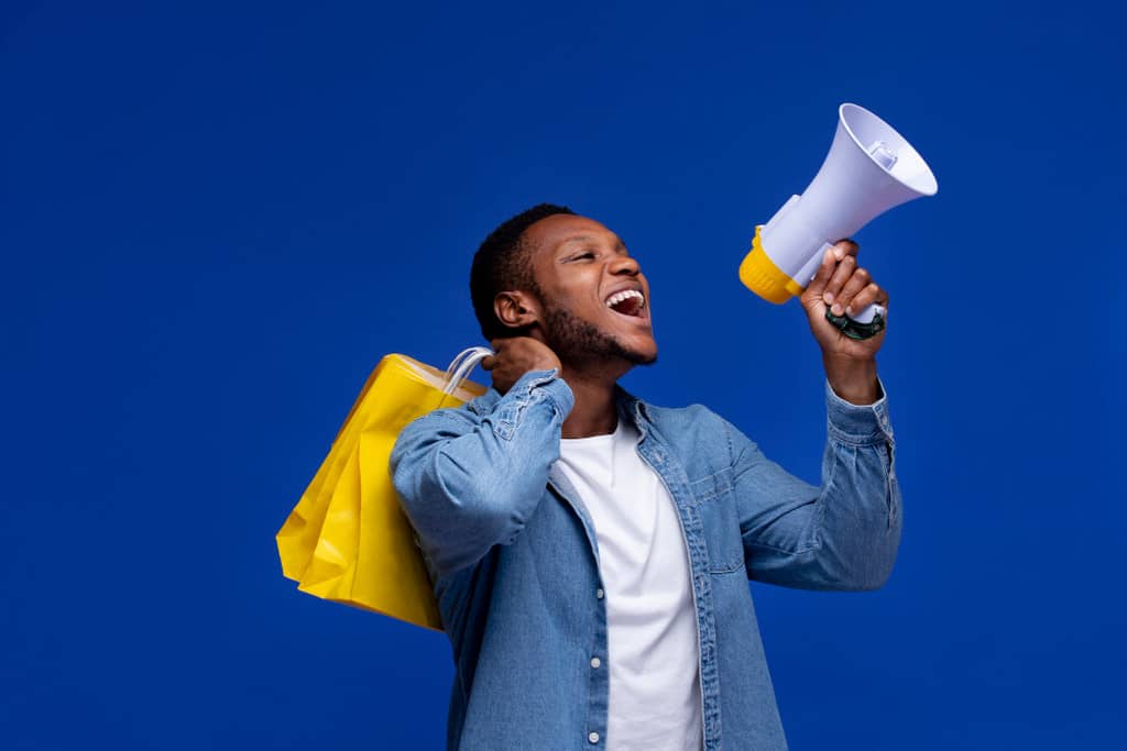 Homem segurando sacola de compras nas costas enquanto fala em um megafone, representando campanha promocional personalizada